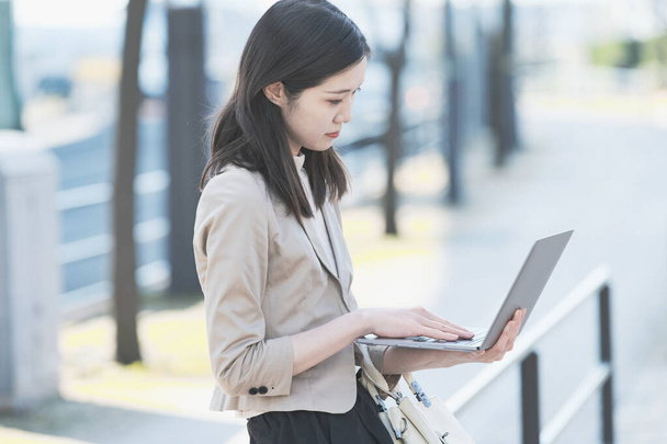 Aasian (japanilainen) naispuolinen toimistotyöntekijä työskentelee ulkona kannettavan tietokoneen kanssa
 - Valokuva, kuva