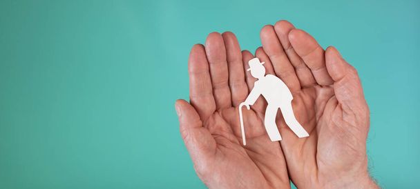 Концепция страхования по старости с бумагой пожилого человека в руках на бирюзовом фоне - Фото, изображение