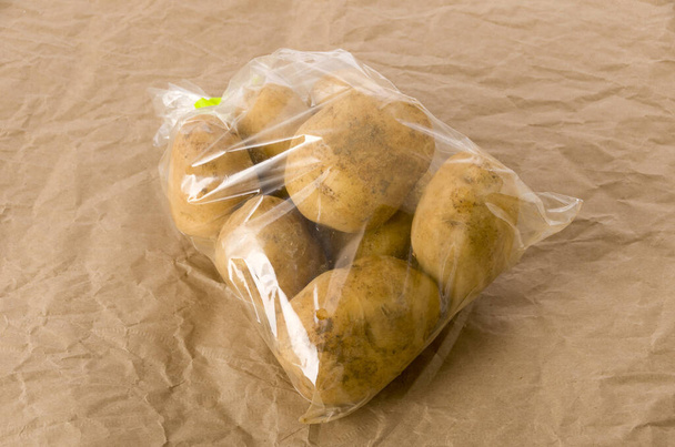 πατάτα σε πλαστική σακούλα σε καφέ φόντο χαρτί  - Φωτογραφία, εικόνα
