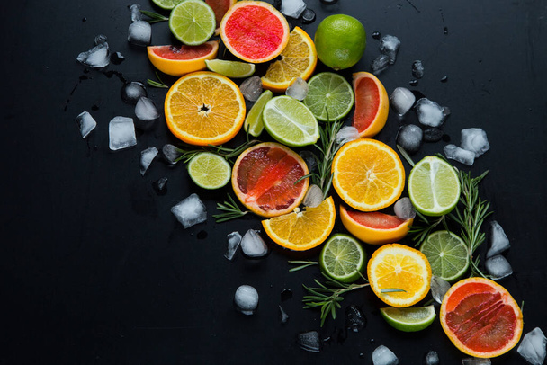 Friss gyümölcsdarabolás. Citrom, narancs, gránátalma jéggel a fekete fa asztalon  - Fotó, kép
