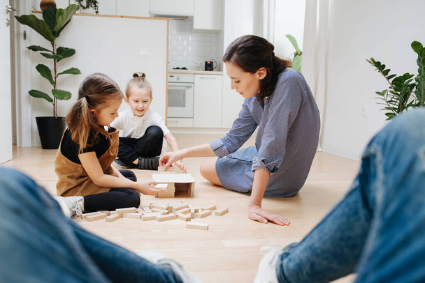 Point of view photo. Father looks how mom and kids playing with wooden blocks, building simple house during isolation at home. - Foto, Imagem