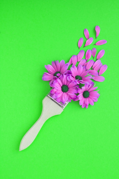 Creative flowers composition. Paintbrush  with pink flowers  on the green background. Location vertical. Top view. Copy space. - Foto, Bild