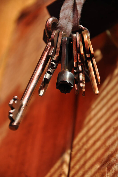 Joukko avaimia roikkuu likainen nauha puinen tausta. Vintage avaimet loistaa auringonvalossa varjo raidat puulankku tausta. Antiikkiesineitä. Vanhat erikokoiset metalliavaimet
 - Valokuva, kuva