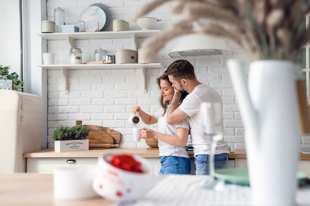 The guy gently hugs the girl who is preparing coffee for him - Fotoğraf, Görsel