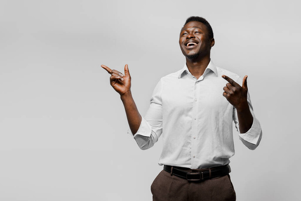Exitoso empresario africano sobre fondo blanco. Negocios en cuarentena covid-19 punto. Hombre negro sonríe y señala los dedos al lado izquierdo vacío
 - Foto, Imagen