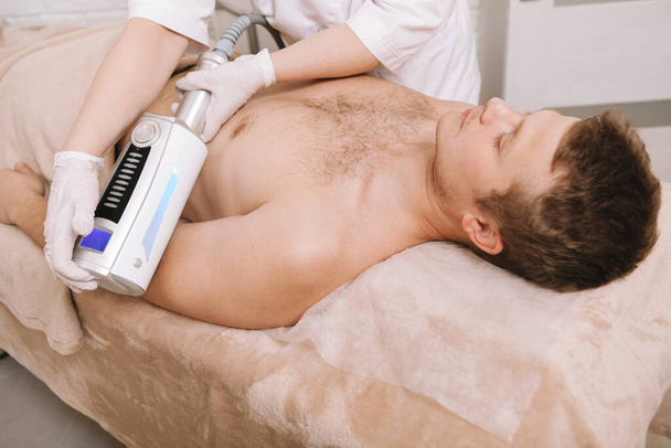 Unrecognizable cosmetologist massaging arm of a male client using  massage apparatus - Fotó, kép