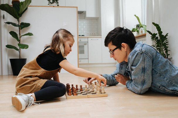 Happy father and his little daughter playing chess on a kitchen floor at home. Side view - Foto, Imagem