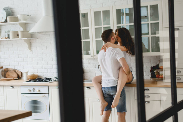 The guy passionately kisses the girl sitting on the kitchen table - Foto, Imagem