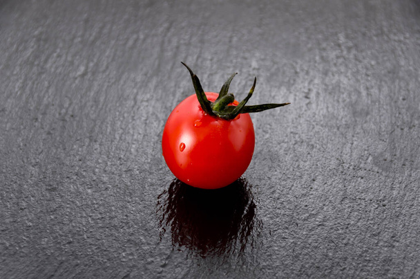 Świeże czerwone pomidory wiśniowe na czarnym kamiennym talerzu - Zdjęcie, obraz