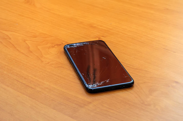 Blick auf den geknackten Bildschirm eines Smartphones auf einem Schreibtisch im Home Office. - Foto, Bild