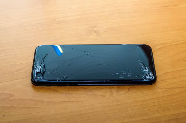 Widok na pęknięty ekran smartfona na biurku w domu biurowym. - Zdjęcie, obraz