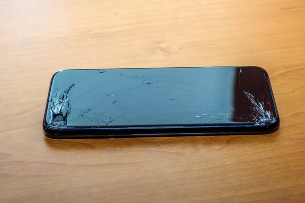 Bekijk op een gekraakt scherm van een smartphone op een bureau in een thuiskantooromgeving. - Foto, afbeelding