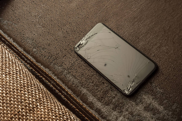 View on a cracked screen of a smartphone on an antique retro leather sofa. - Valokuva, kuva