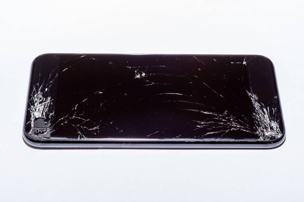 Blick auf den geknackten Bildschirm eines Smartphones auf weißem Hintergrund. - Foto, Bild