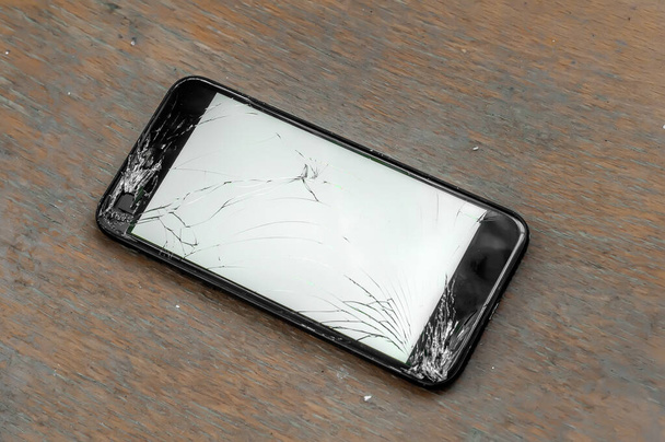 View on a cracked screen of a smartphone on a wooden surface. - Photo, Image