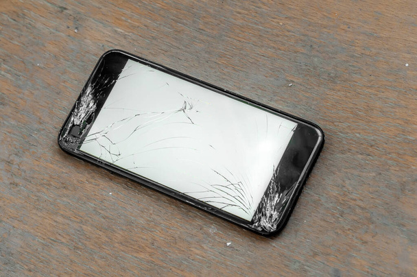 Widok na pęknięty ekran smartfona na drewnianej powierzchni. - Zdjęcie, obraz