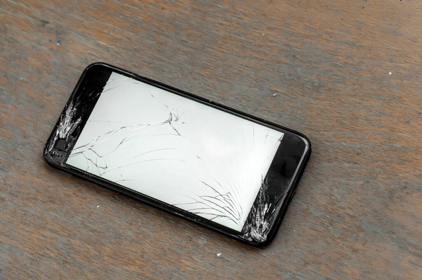 View on a cracked screen of a smartphone on a wooden surface. - Photo, Image