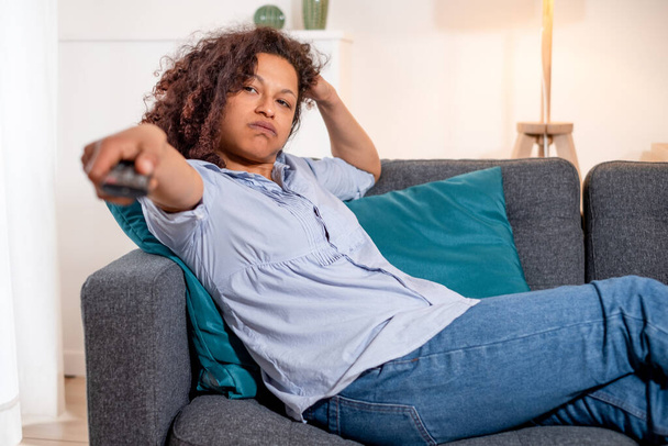 Μαύρη κουρασμένη γυναίκα χαλαρώνει στο σπίτι βλέποντας τηλεόραση - Φωτογραφία, εικόνα