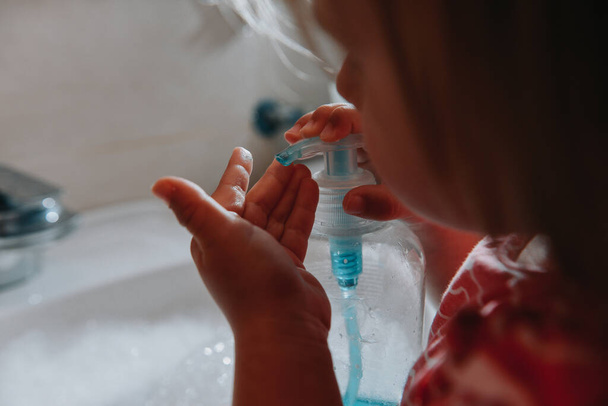 Cute little toddler girl press bottle dispenser with liquid soap for washing her hands in a bathroom. Hygiene concept showing prevention of infection and viruses such as flu and covid-19 - Foto, Imagen