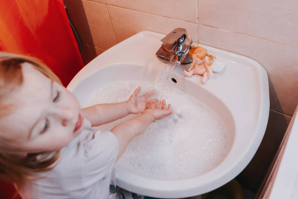 Cute little toddler girl washing her hands in a bathroom. Hygiene concept showing prevention of infection and viruses such as flu and covid-19 - Foto, Imagen