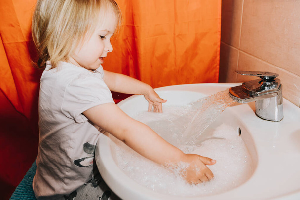 Cute little toddler girl washing her hands in a bathroom. Hygiene concept showing prevention of infection and viruses such as flu and covid-19 - Foto, Imagen