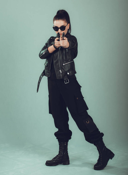 Shot of a sexy military woman posing with guns,in a black jacket,black glasses in the eyes, - Φωτογραφία, εικόνα