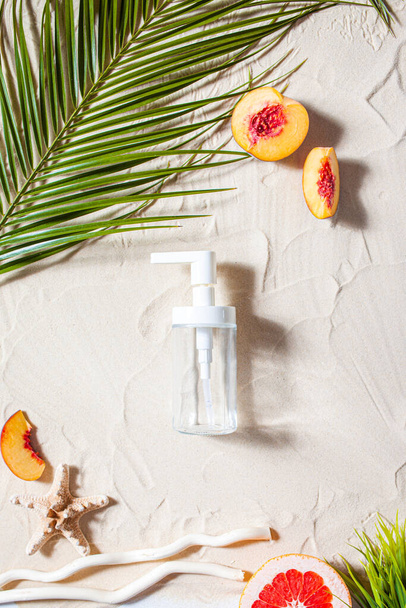 Safe sun. Skin care. A transparent bottle lies on the beach sand, surrounded by vibrant fruits, corals, and palm leaves. - Φωτογραφία, εικόνα