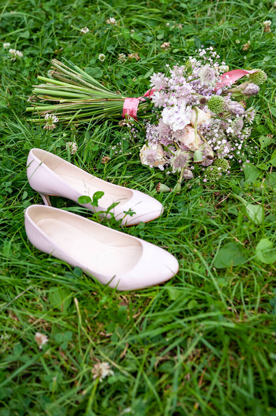 Düğün ayakkabıları ve yeşil çimen arka planında mor beyaz ve pembe boho buketi. Güzel bir buket yabani çiçek ve pembe topuklu ayakkabı. Vintage Boho düğün süsleme çiçeklerini vurdu. Haşhaş, sarımsak, gül çiçeği. - Fotoğraf, Görsel