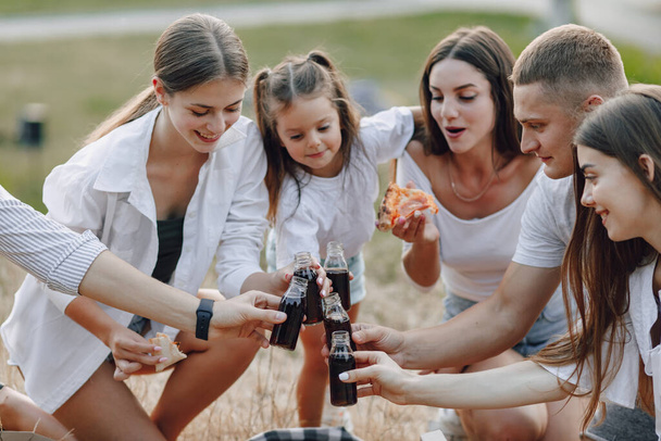 piknikowi przyjaciele z pizzą i piciem i jedzeniem na zdrowie, ciepły słoneczny dzień, zachód słońca, towarzystwo, zabawa, pary i mama z dzieckiem - Zdjęcie, obraz