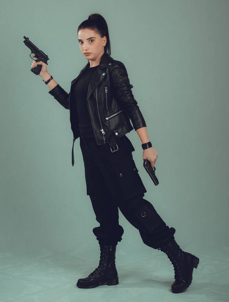 Shot of a sexy military woman posing with guns,in a black jacket, - Фото, зображення