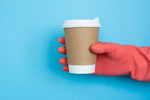 Hand with coffee paper cup, coronavirus protection. Mockup of female hand holding a coffee paper cup. Copy space. Coffee cup in hand with medical gloves isolated on blue background. - Foto, immagini