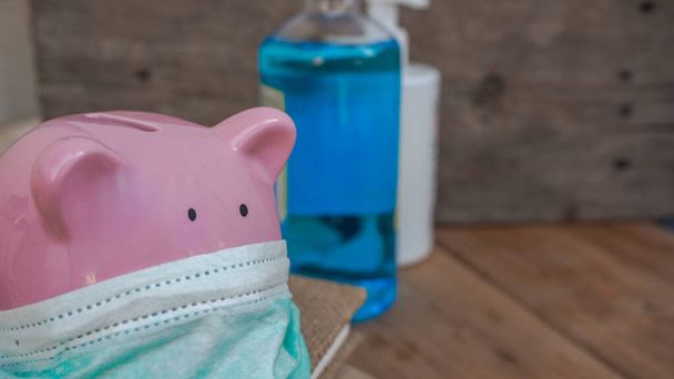 Close up of piggy bank, wearing protective face mask in black background. Money saving concept in time of coronavirus, crisis pandemic. - Foto, immagini