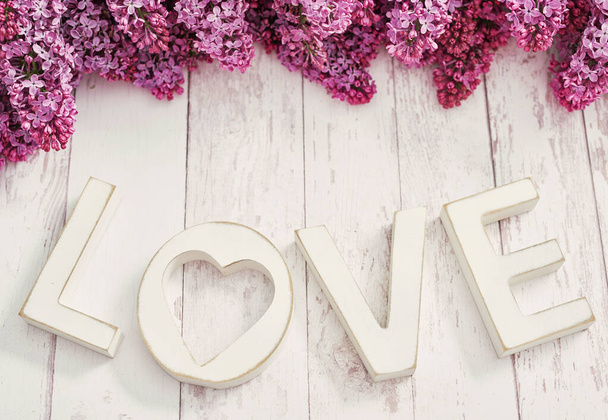 Text LOVE made from wooden letters and lilac flowers.Happy birthday greeting card.Hello spring and summer. Greeting card for Women's Day and Mother's Day.Spring season, copy space.Romantic background - Foto, immagini