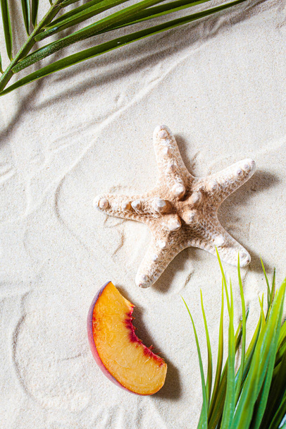 Beach vacation. A palm leaf, starfish, and white tree branch and juicy fruits lie on white fine sand. Desktop wallpaper. - 写真・画像