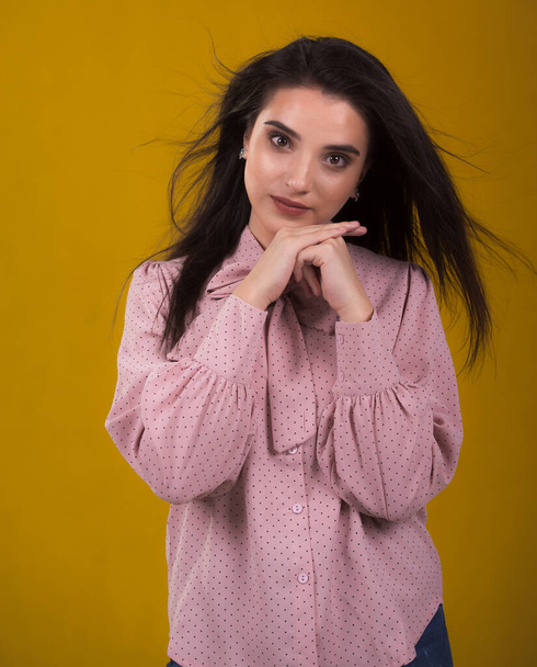 young beautiful brunette model in pink sweater,laughs and shakes his hair in the air,yellow background on the back,caressing looks very sweet camera,posing in studio, - Foto, afbeelding
