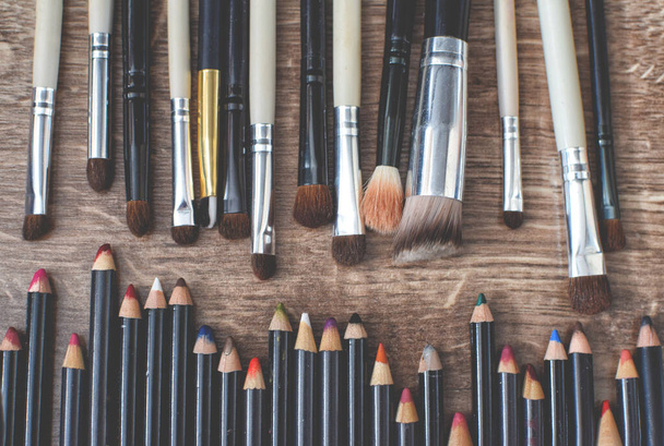 Cosmetic brushes and pencils lie on a wooden brown floor - 写真・画像