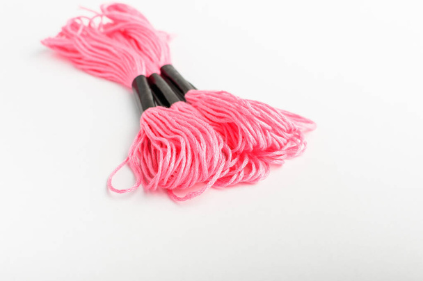 Три ярко-розовых нити для вышивки, изолированные на белом столе, с видом сверху или плоским слоем текстильных материалов
 - Фото, изображение