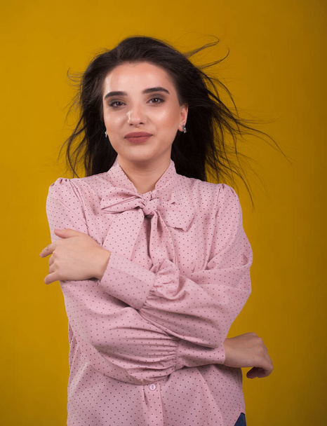 young beautiful brunette model in pink sweater,laughs and shakes his hair in the air,yellow background on the back,caressing looks very sweet camera,posing in studio, - Фото, изображение