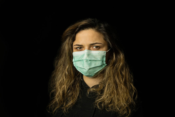 Studioporträt einer jungen Frau mit Gesichtsmaske, die in die Kamera blickt, aus nächster Nähe, isoliert auf schwarzem Hintergrund. - Foto, Bild