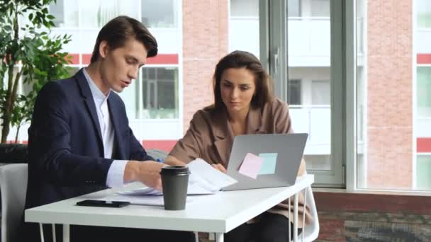 A man and a woman work at a laptop in a modern office. teamwork concept 4K. Deadline, employees desk with coffee and documents - Materiał filmowy, wideo