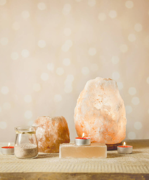 Himalayan Salt Soap Bar, rosa Steinsalzlampe eingeschaltet und Salzkerzenhalter, mit brennenden Kerzen im Inneren, Glas mit Salzkörnern auf hellem Bokeh-Hintergrund, Studio. Beruhigendes Zen-Stimmungskonzept. - Foto, Bild