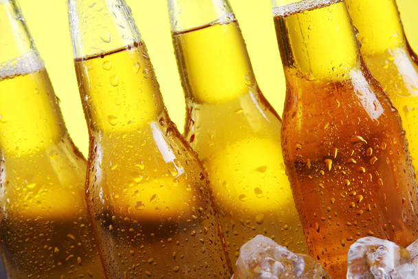Botellas de cerveza fría y fresca con hielo sobre fondo amarillo
 - Foto, Imagen