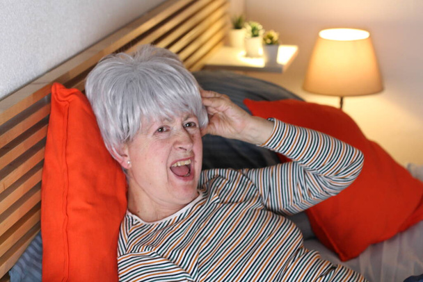 成熟した白髪の女性は自宅で隔離中にベッドに寝そべって - 写真・画像