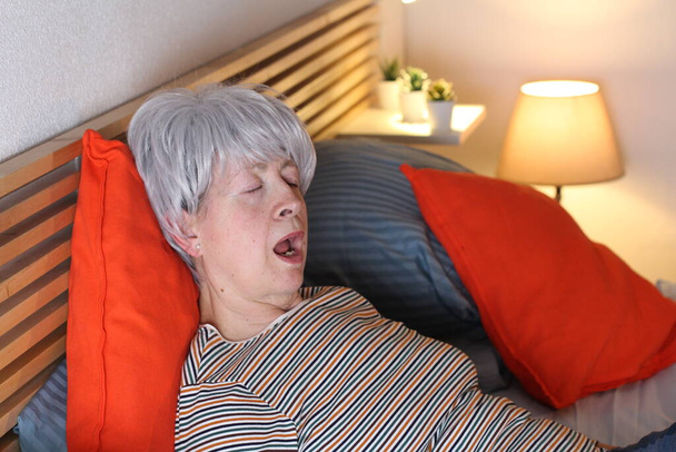 mature femme aux cheveux gris bâillant tout en se relaxant au lit pendant l'isolement à la maison
 - Photo, image