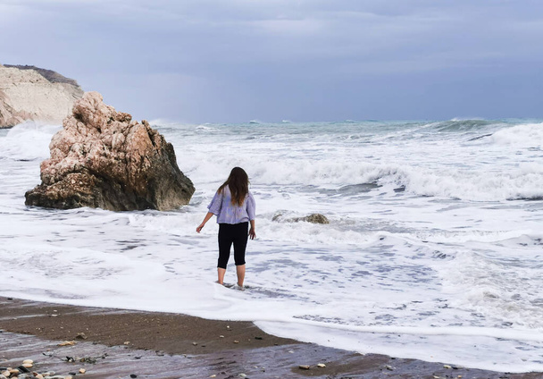 Μη αναγνωρίσιμο άτομο που απολαμβάνει το θυελλώδες θαλασσινό τοπίο με τα κύματα του ανέμου. Βράχος της Αφροδίτης, ακτογραμμή Πέτρας του Ρωμιού στην περιοχή Πάφος στην Κύπρος - Φωτογραφία, εικόνα
