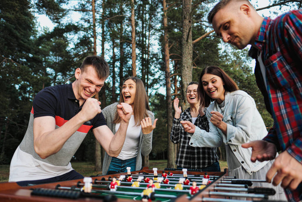 Friends play table football or kicker outdoors. Players and fans rejoice in the victory. - Foto, Imagen