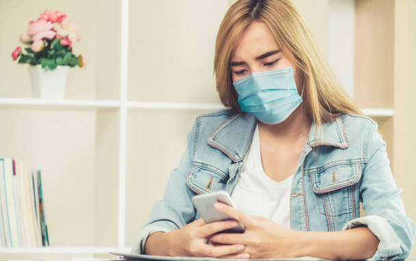 Quarantined woman working at home wearing face mask protect from Coronavirus. Concept of social distancing to stop spreading of Coronavirus Disease or COVID-19. - Photo, image