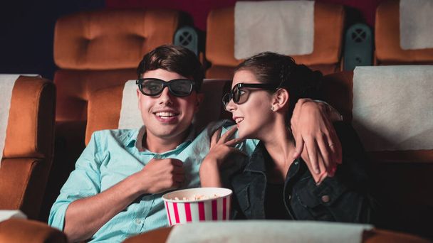 Man and woman in the cinema watching a movie with 3D glasses. with interest looking at the screen, exciting and eating popcorn - Photo, Image