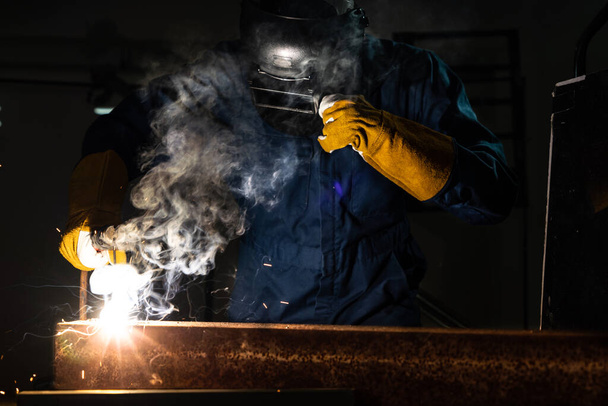 Metal welder working with arc welding machine to weld steel at factory while wearing safety equipment. Metalwork manufacturing and construction maintenance service by manual skill labor concept. - Fotoğraf, Görsel