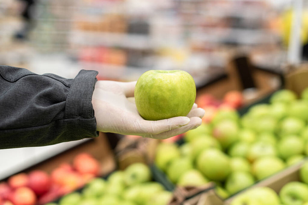 Man courier in protective rubber gloves choosing green apple for online shopper in grocery store, supermarket. Protection from bacteria and virus. Coronavirus. contact less safe delivery - Foto, afbeelding